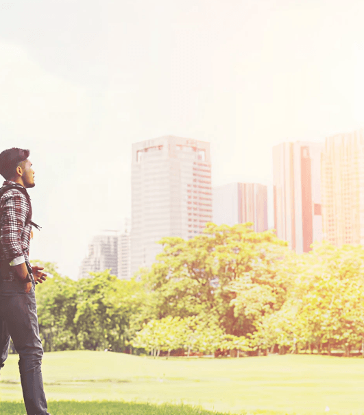 A resident looking up at city high-rises from a sunlit park